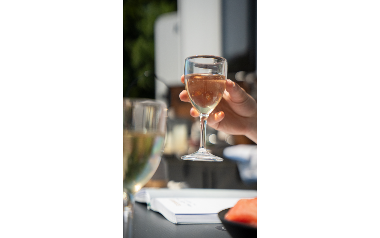 Hand houdt een glas met roze drank boven een tafel met glazen en documenten
