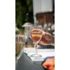 Hand houdt een wijnglas met rosékleurige drank, vage tafel en stoel buiten op de achtergrond