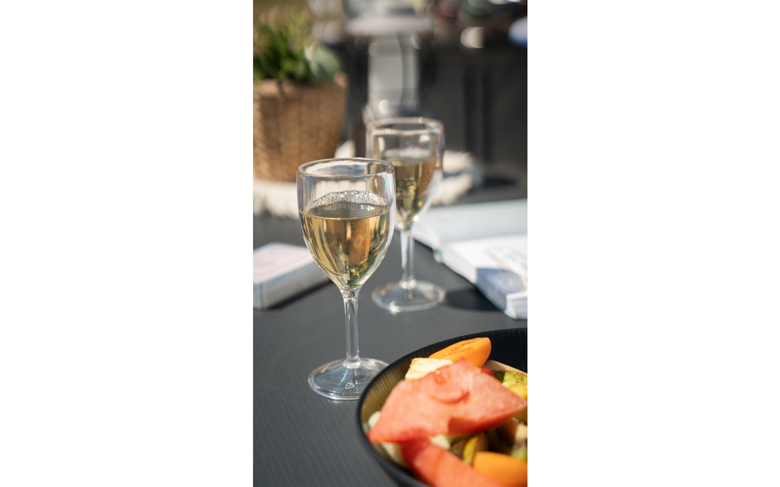 Zwei Weingläser mit weißem Wein auf einem Tisch, davor ein Teller mit Melonenstücken