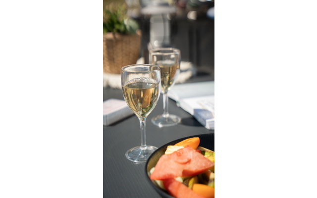 Zwei Weingläser mit weißem Wein auf einem Tisch, davor ein Teller mit Melonenstücken