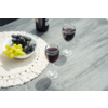 Dos copas de vino tinto en una mesa de madera; junto a ellas un cuenco con uvas verdes y negras sobre un salvamanteles de ganchillo y una botella de vino en el borde