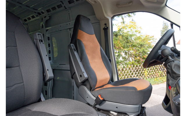 Intérieur d'une camionnette avec deux sièges avant, accoudoirs, volant, cloison et une fenêtre donnant sur des arbres et une clôture