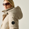 Person mit Sonnenbrille, beige Steppjacke mit Kapuze und rundem Aufnäher auf dem Ärmel