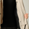 Teilansicht einer Person in schwarzem Pullover, die eine offene beige Jacke mit dunklem Innenfutter und Reißverschluss hält