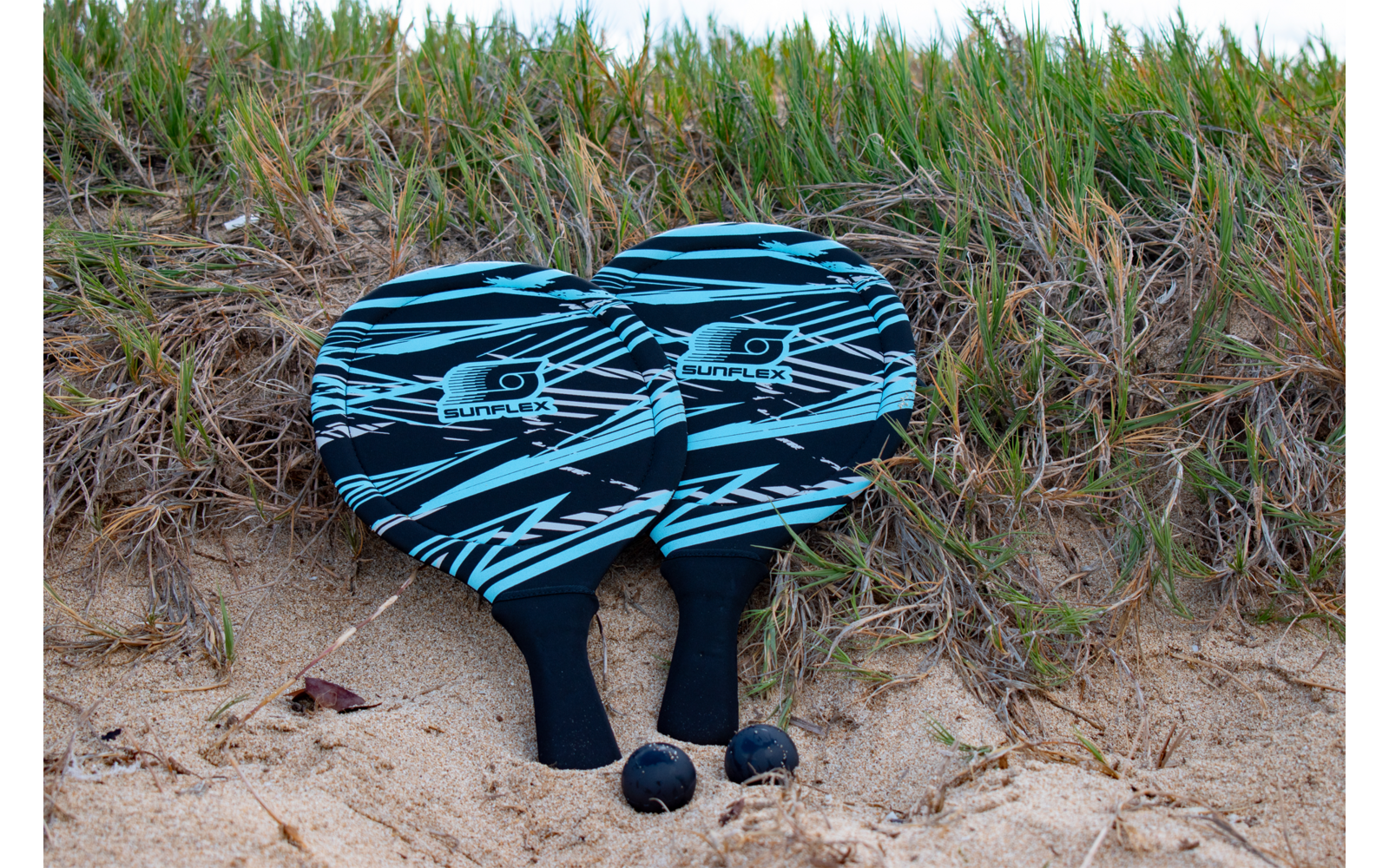 Zwei schwarze Füße ragen unter einem blauen und schwarzen gestreiften Handtuch hervor, im Hintergrund Gras und Sand