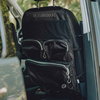 Schwarze Stoff-Organizer-Tasche mit dem Schriftzug "BUSBOXX" an der Rückseite eines Fahrzeugsitzes, mehrere Reißverschlusstaschen, Kopfstützenriemen und Autofenster mit grüner Außenansicht