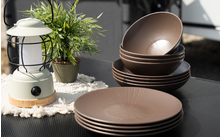 Plusieurs assiettes et bols marron sur une table noire à côté d'une lanterne blanche et d'une petite plante verte en pot