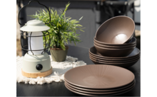 Plusieurs assiettes et bols marron sur une table noire à côté d'une lanterne blanche et d'une petite plante verte en pot