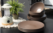 Plusieurs assiettes et bols marron sur une table noire à côté d'une lanterne blanche et d'une petite plante verte en pot