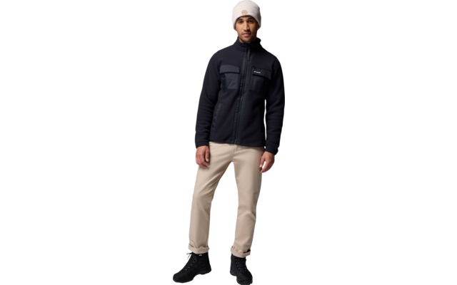 Ein Mann mit weißer Mütze, dunkelblauer Jacke und beiger Hose steht