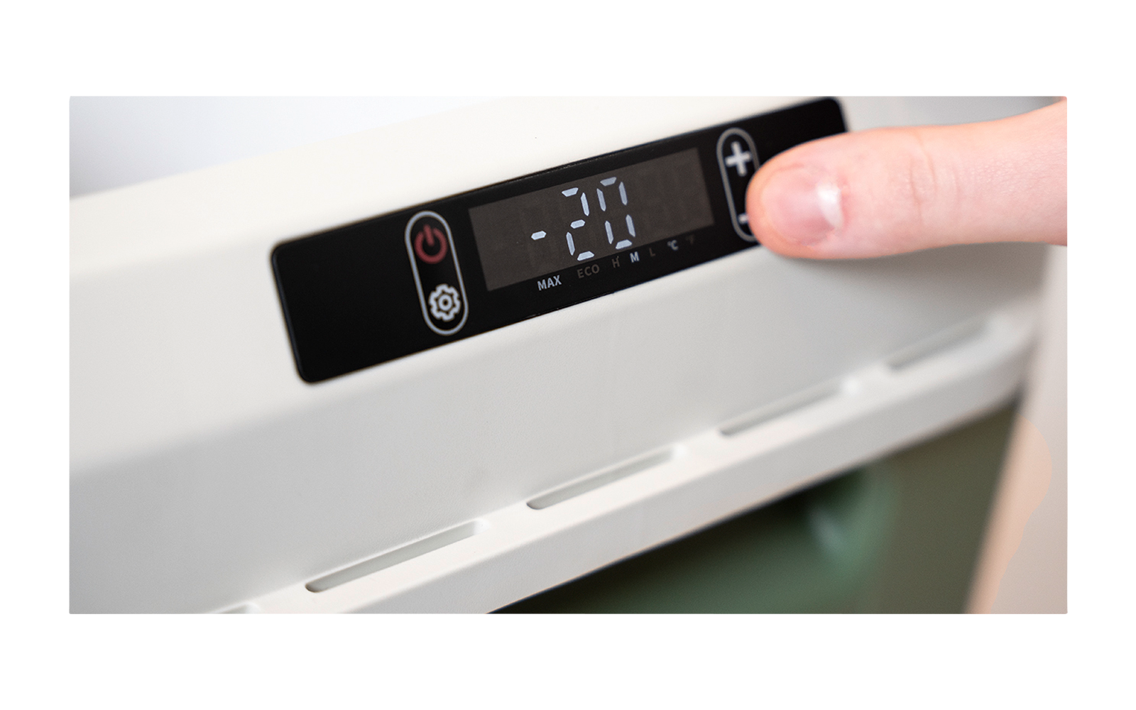 Rechte Hand, Daumen drückt Knopf auf schwarzem Bedienfeld eines weißen Geräts; digitale Anzeige zeigt "-70", zwei Symbole neben dem Display, Belüftungsschlitze darunter