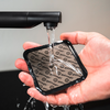 Hand houdt een vierkant zwart pad met herhaalde tekst "gelmags" onder stromend water uit een kraan