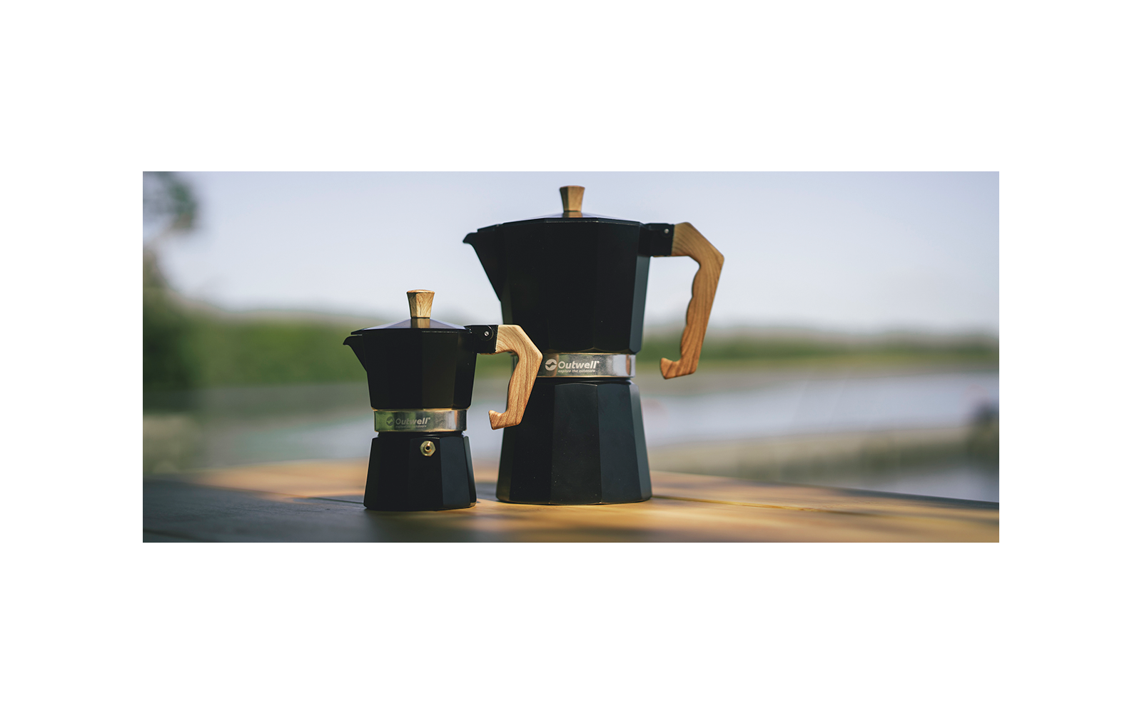 Twee zwarte espressomachines op een houten plank met een wazige achtergrond van water en bomen