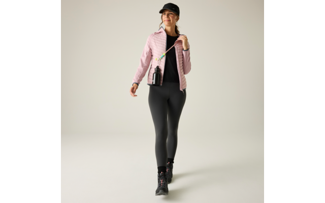 Frau in Sportkleidung geht, trägt schwarze Kappe, rosa gesteppte Jacke, schwarzes Oberteil, schwarze Leggings und schwarze Wanderschuhe; schwarze Trinkflasche hängt an einem Schulterband