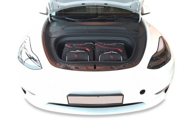 Coffre avant ouvert d'une voiture blanche contenant deux sacs de voyage noirs avec bordure rouge