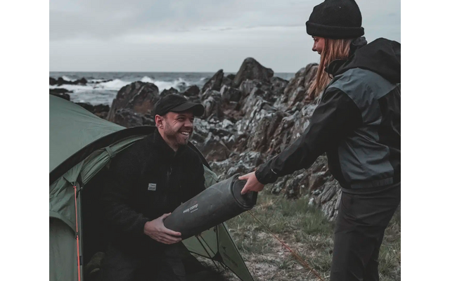 Zwei Männer in Outdoor-Kleidung beim Umgang mit einem Zeltausleger am Meer mit Felsen im Hintergrund