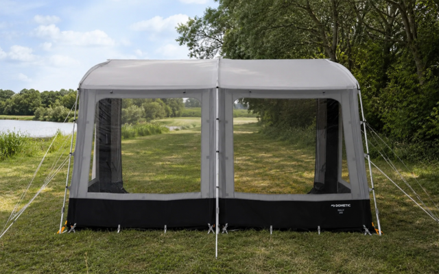 Gray and black tent with two large mesh windows, pitched on grass next to a lake, trees in the background