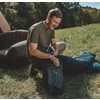 Ein Mann sitzt auf einer Wiese neben einem Zelt und schaut in einen Rucksack