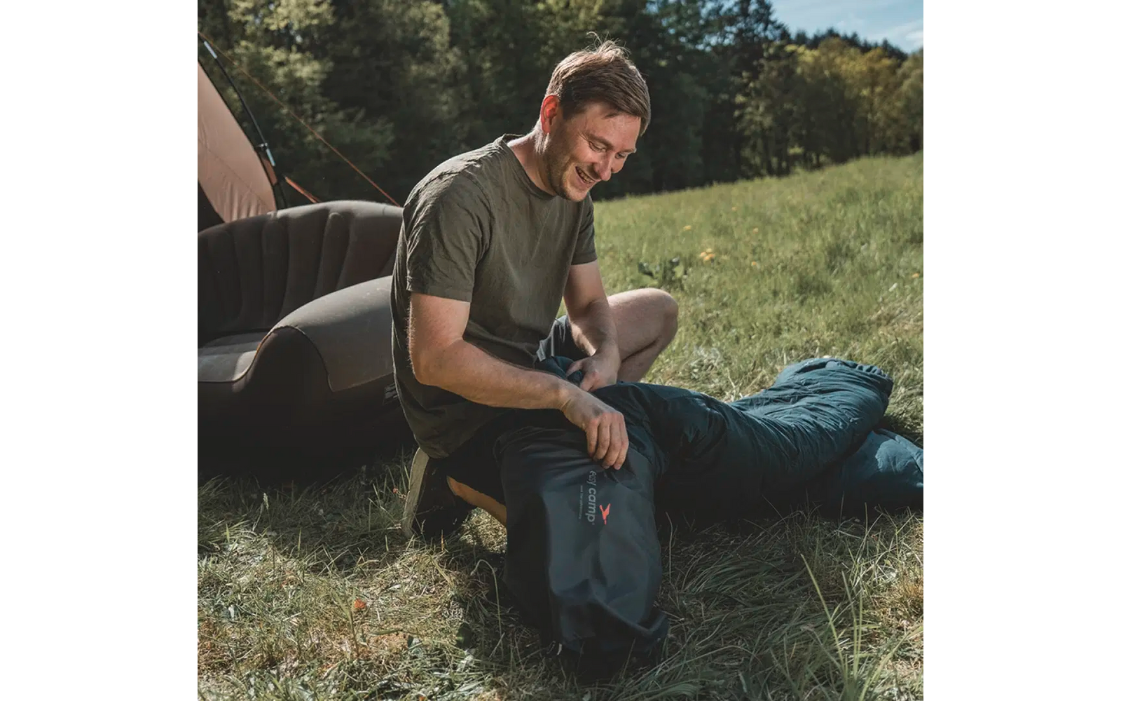 Ein Mann sitzt auf einer Wiese neben einem Zelt und schaut in einen Rucksack