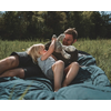 Zwei Frauen liegen auf einer Decke in einer Wiese, eine Frau hält ein Handy und die andere lacht