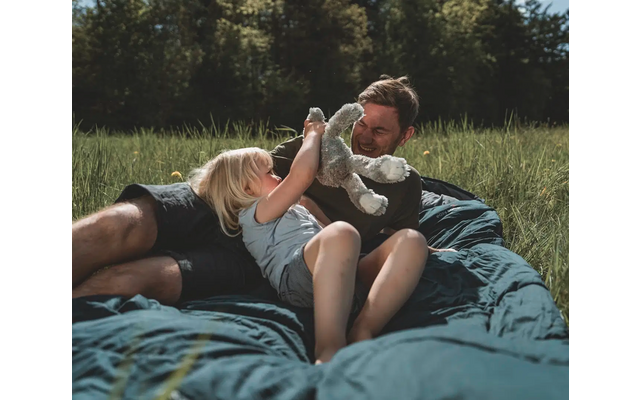 Zwei Frauen liegen auf einer Decke in einer Wiese, eine Frau hält ein Handy und die andere lacht