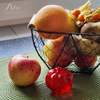 Verschiedene Früchte, darunter ein Apfel und eine Granatapfelflasche, neben einem Drahtkorb mit Grapefruits und anderem Obst auf einer Tischoberfläche