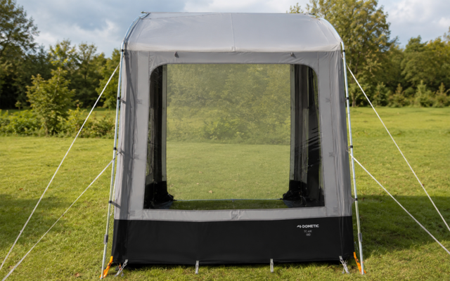 Rectangular gray tent with large front mesh panel, guy lines and pegs on grass, trees in the background