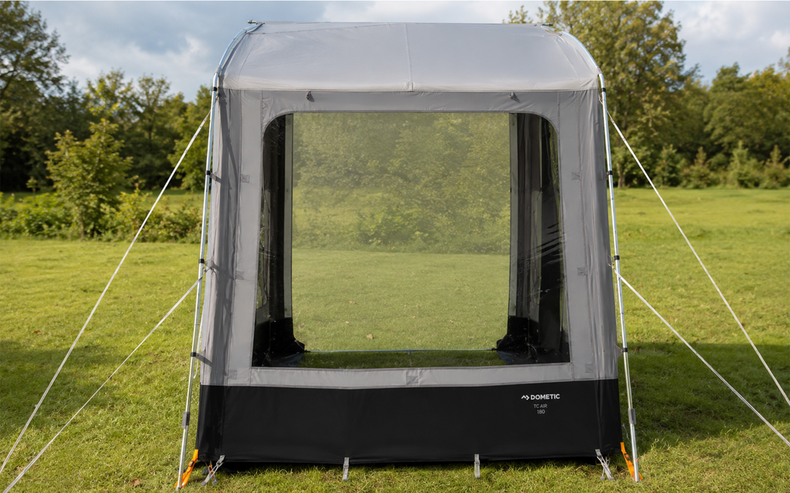 Rectangular gray tent with large front mesh panel, guy lines and pegs on grass, trees in the background