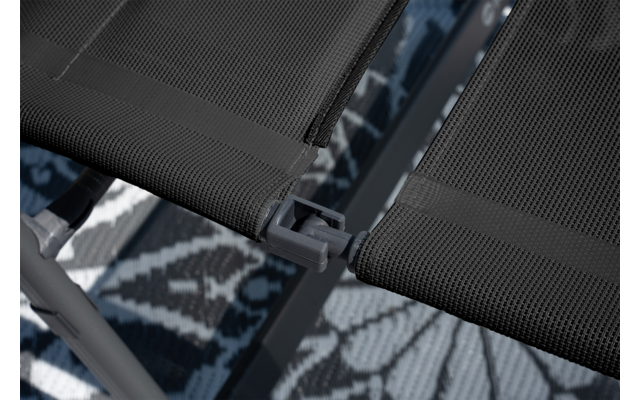 Close-up van twee zwarte gaasstofpanelen die met een grijs kunststof verbindingsstuk aan een donker metalen frame zijn verbonden; patroon vloerkleed eronder