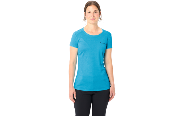 Frau steht frontal vor weißem Hintergrund, trägt blaues T‑Shirt mit kurzen Ärmeln und schwarze Hose, Hände seitlich