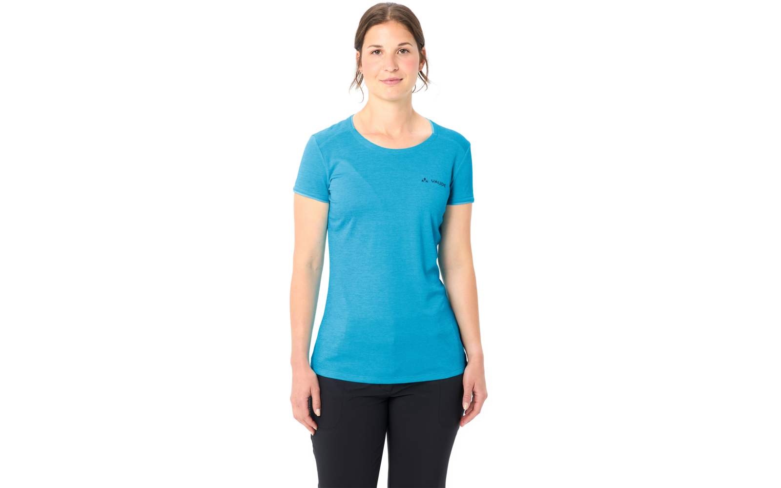 Frau steht frontal vor weißem Hintergrund, trägt blaues T‑Shirt mit kurzen Ärmeln und schwarze Hose, Hände seitlich