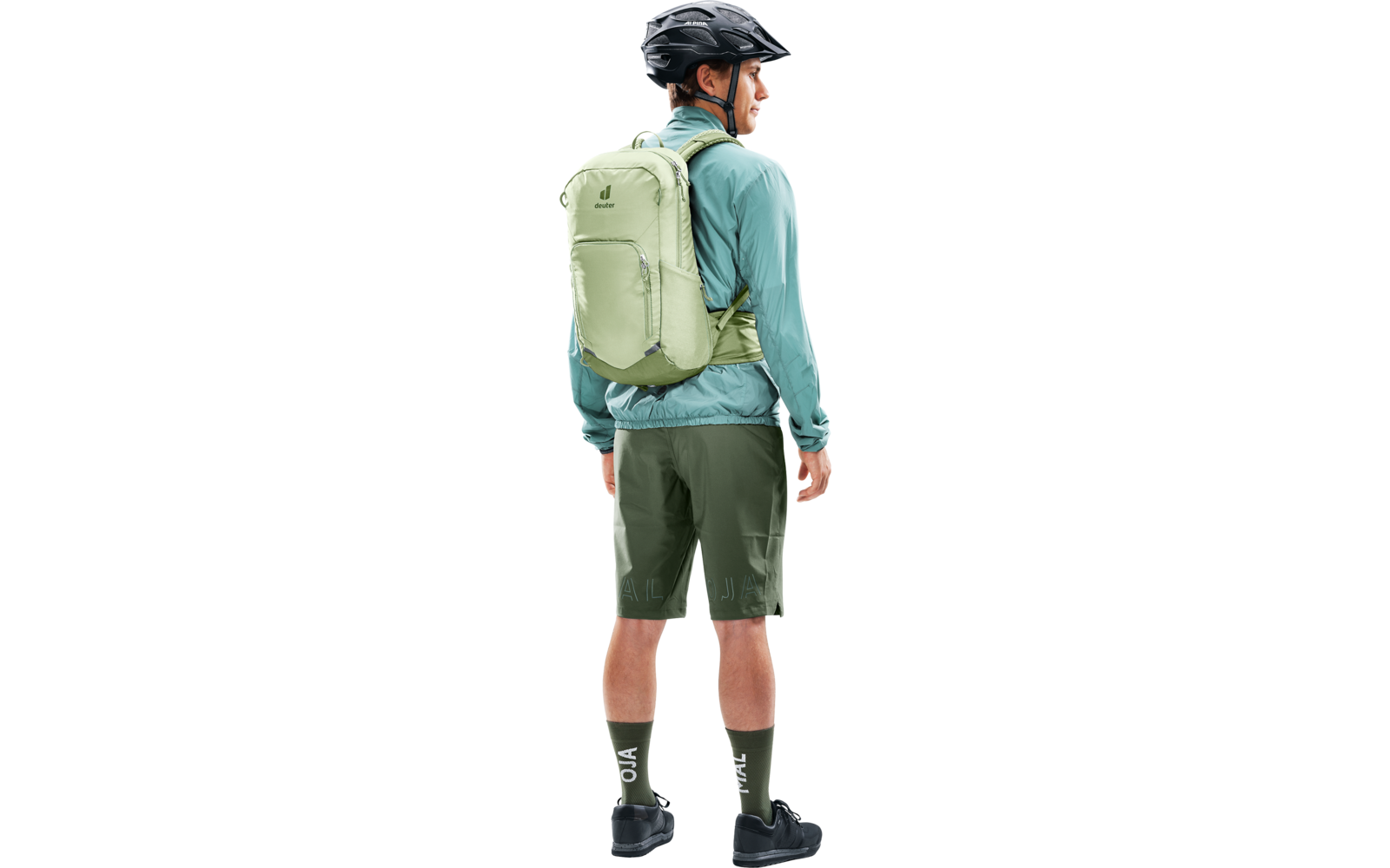 Seitenansicht einer Person mit Fahrradhelm, hellgrünem Rucksack, türkiser Jacke, dunkelgrünen Shorts, grünen Socken und schwarzen Schuhen, nach rechts blickend