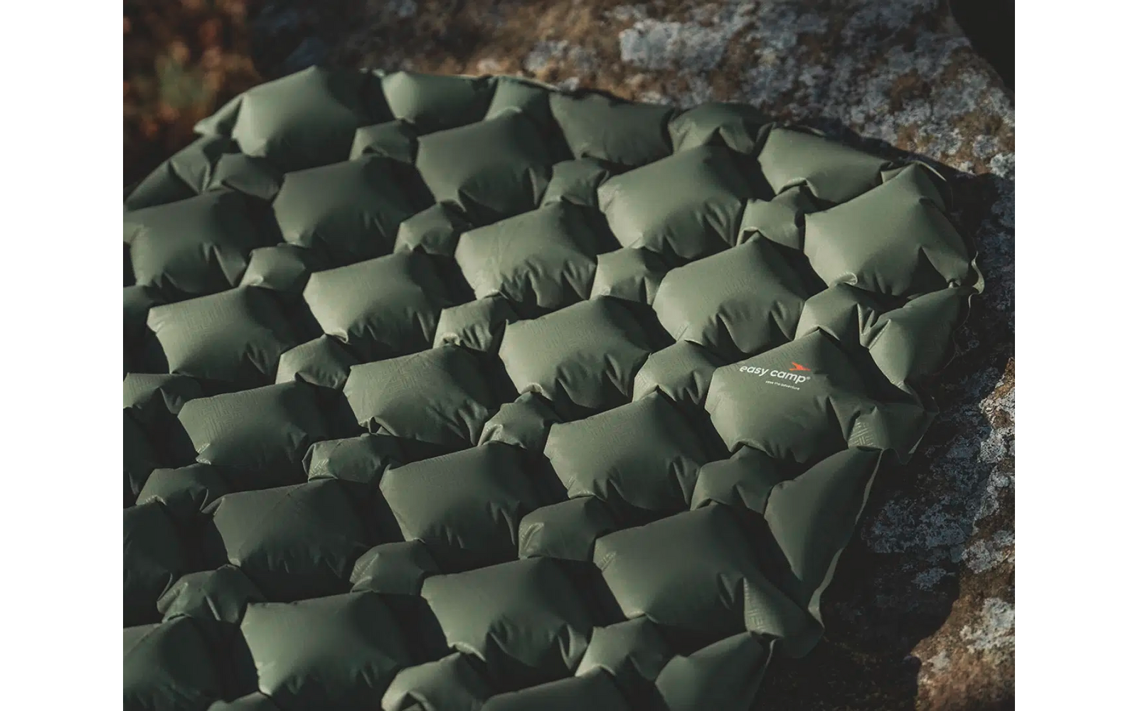 Grüner, gepolsterter Outdoor-Sitzsack auf grauem Boden neben Steinmauer