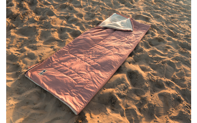 Sac de couchage rectangulaire orange avec doublure intérieure blanche visible, posé sur du sable ; aucune personne visible