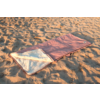 Sac de couchage rose avec doublure en polaire claire, ouvert posé sur du sable ondulé
