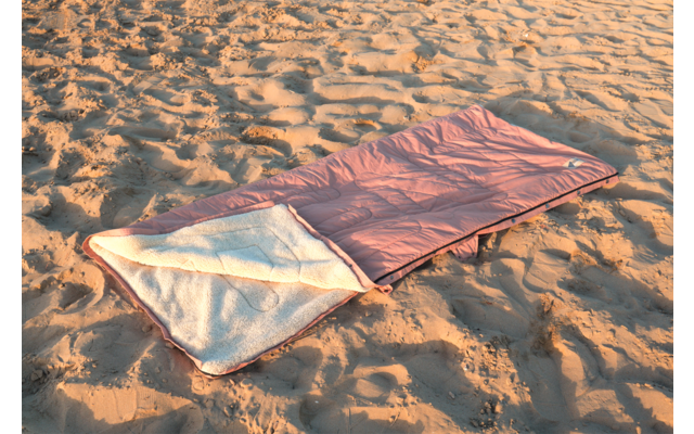Sac de couchage rose avec doublure en polaire claire, ouvert posé sur du sable ondulé