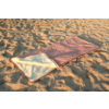 Sac de couchage rose ouvert avec doublure blanche posé sur du sable avec empreintes de pas et ondulations
