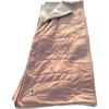 Sac de couchage rose à doublure plus claire, replié en haut, posé à plat sur du sable avec des empreintes et des ombres