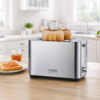 Edelstahl-Toaster mit zwei hochstehenden Toastscheiben auf der Arbeitsplatte; daneben Teller mit bestrichenem Toast und kleines Marmeladenglas; heller, unscharfer Küchenhintergrund