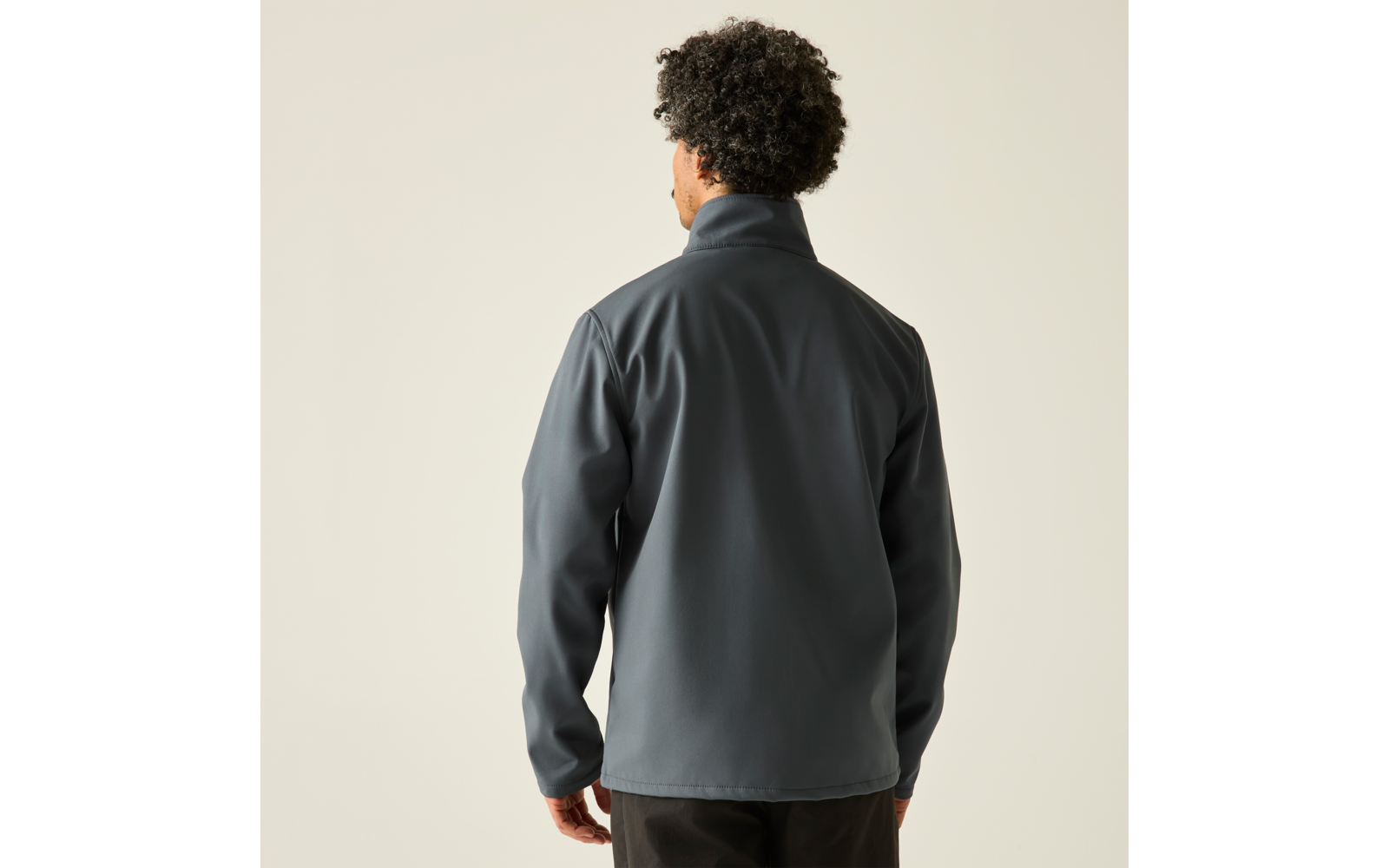 Rückenansicht einer stehenden Person mit lockigem dunklem Haar und grauer Jacke vor hellem Hintergrund