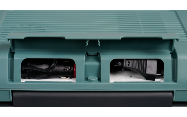 Grün-türkisfarbener Kunststoffkoffer mit zwei rechteckigen Öffnungen; links aufgerolltes schwarzes Kabel mit roten und silbernen Steckern, rechts schwarzes Steckelement mit Kabel und sichtbaren Metallstiften; unterer Bereich dunkelgrau