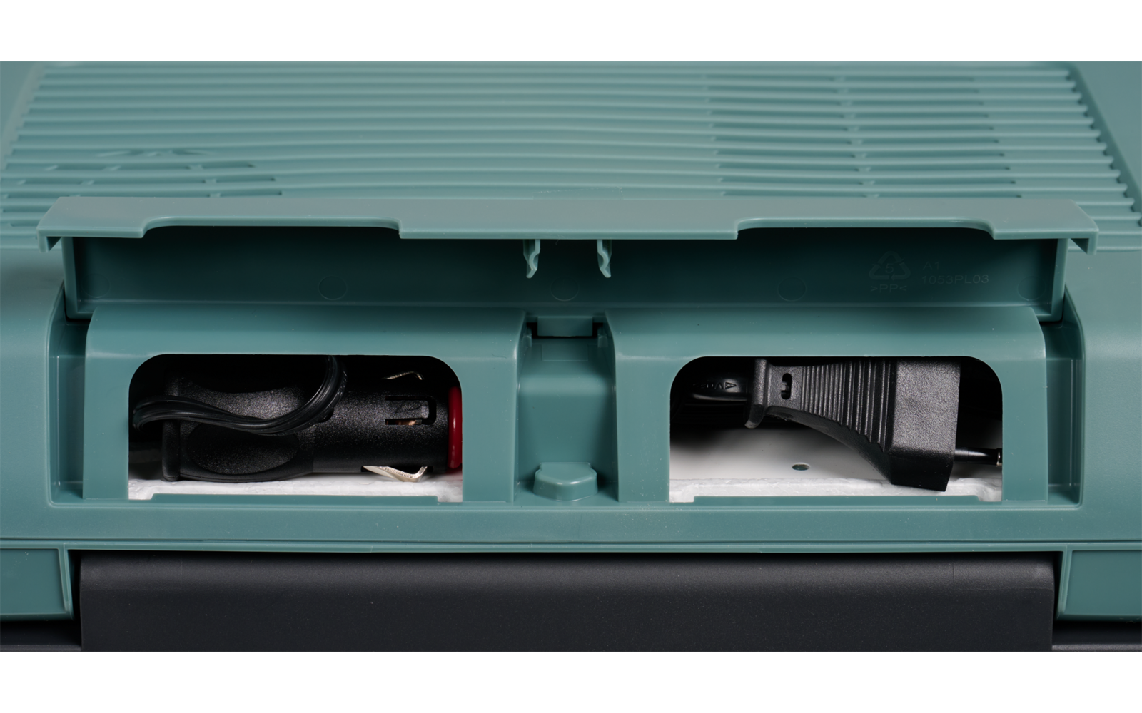 Grün-türkisfarbener Kunststoffkoffer mit zwei rechteckigen Öffnungen; links aufgerolltes schwarzes Kabel mit roten und silbernen Steckern, rechts schwarzes Steckelement mit Kabel und sichtbaren Metallstiften; unterer Bereich dunkelgrau