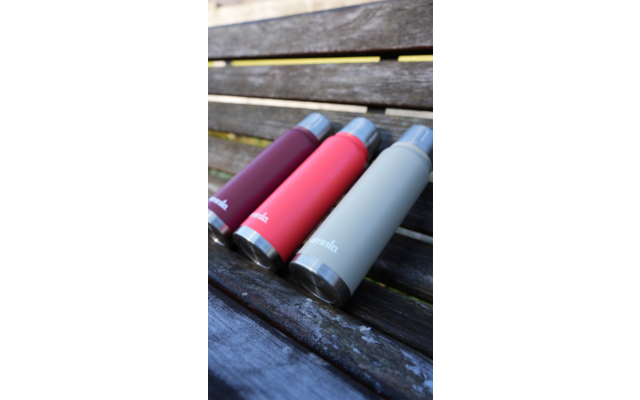 Drie cilindervormige flessen met schroefdoppen in donkerrood, roze en lichtgrijs liggen schuin naast elkaar op een houten bank