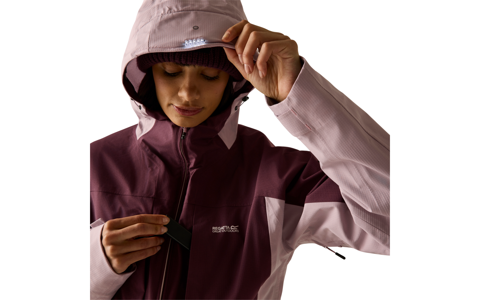Person mit zweifarbiger Kapuzenjacke (hellrosa/dunkelviolett), Kapuze aufgesetzt, eine Hand hält die Krempe, andere Hand an Reißverschluss, weißes Logo auf der Brust