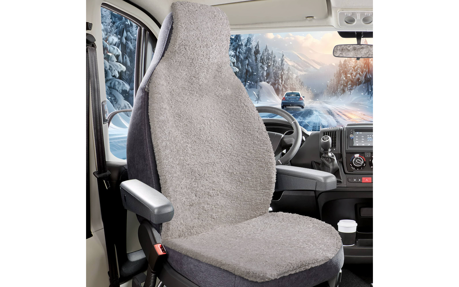 Fahrersitz mit grauem, flauschigem Sitzbezug in einer Lkw‑Kabine; Armlehne, Lenkrad, Armaturenbrett und Becherhalter sichtbar; durch die Seitenscheibe verschneite Straße, Wald, Berge und ein vorausfahrendes Auto
