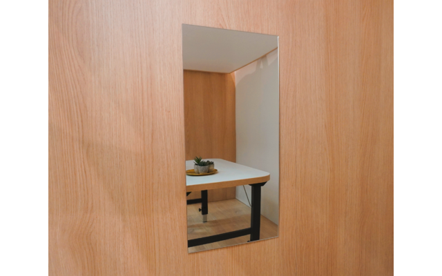 Rechteckiger Spiegel in Holzfläche, Spiegelbild zeigt weißen Tisch mit schwarzen Beinen und kleinen Sukkulenten-Topf, heller Holzboden und Zimmerecke