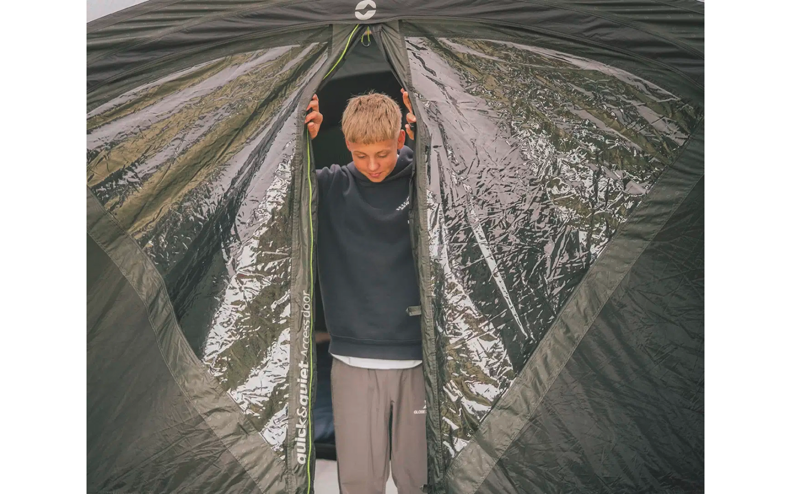 Junge steht vor einem Zelt und hält den Eingang offen