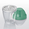 Gobelet en plastique transparent avec insert à grille blanc amovible muni d'une poignée en boucle, à côté d'un couvercle plastique vert en forme de dôme sur une surface réfléchissante