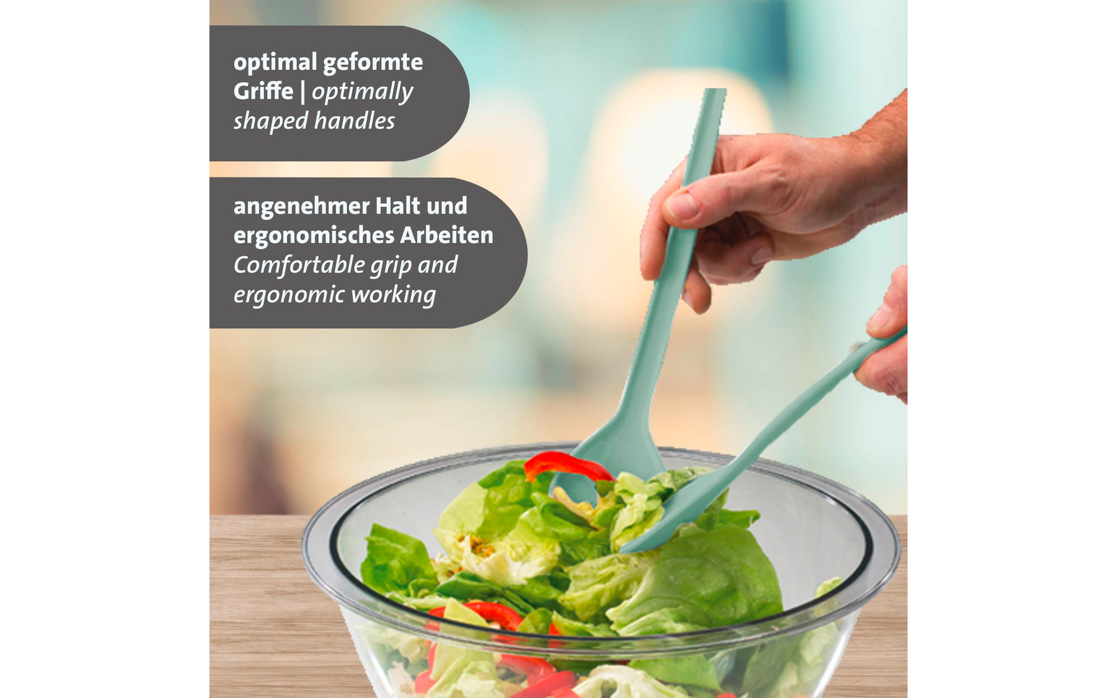 Deux mains tiennent des pinces à salade turquoise au-dessus d'un bol en verre contenant de la salade verte et des lanières de poivron rouge ; deux encadrés de texte en allemand et en anglais