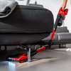 Aspirateur-balai rouge avec éclairage glissé sous un canapé gris en cuir à pieds métalliques; main sur la poignée visible